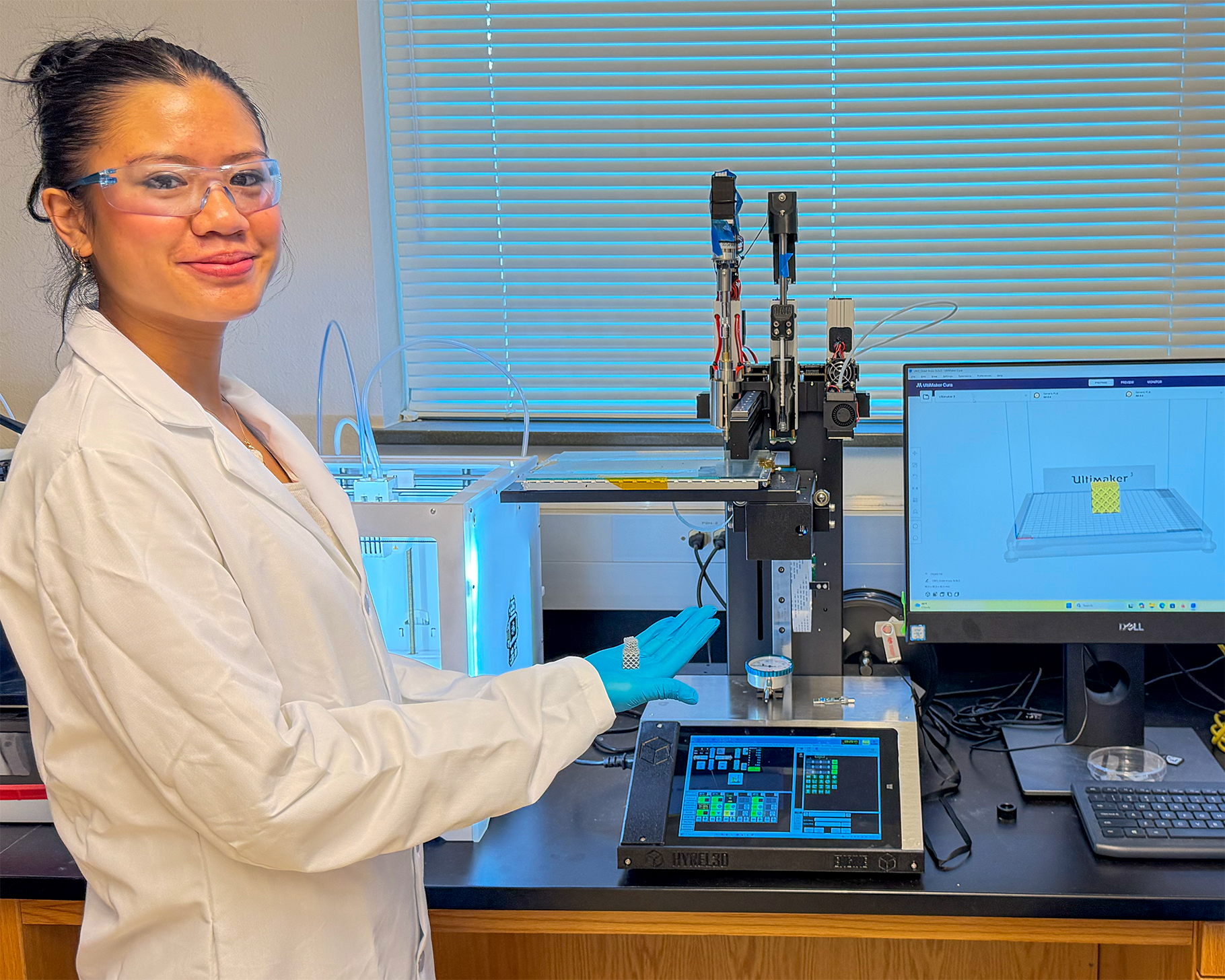 researcher in lab coat holding item next to computer and microscope