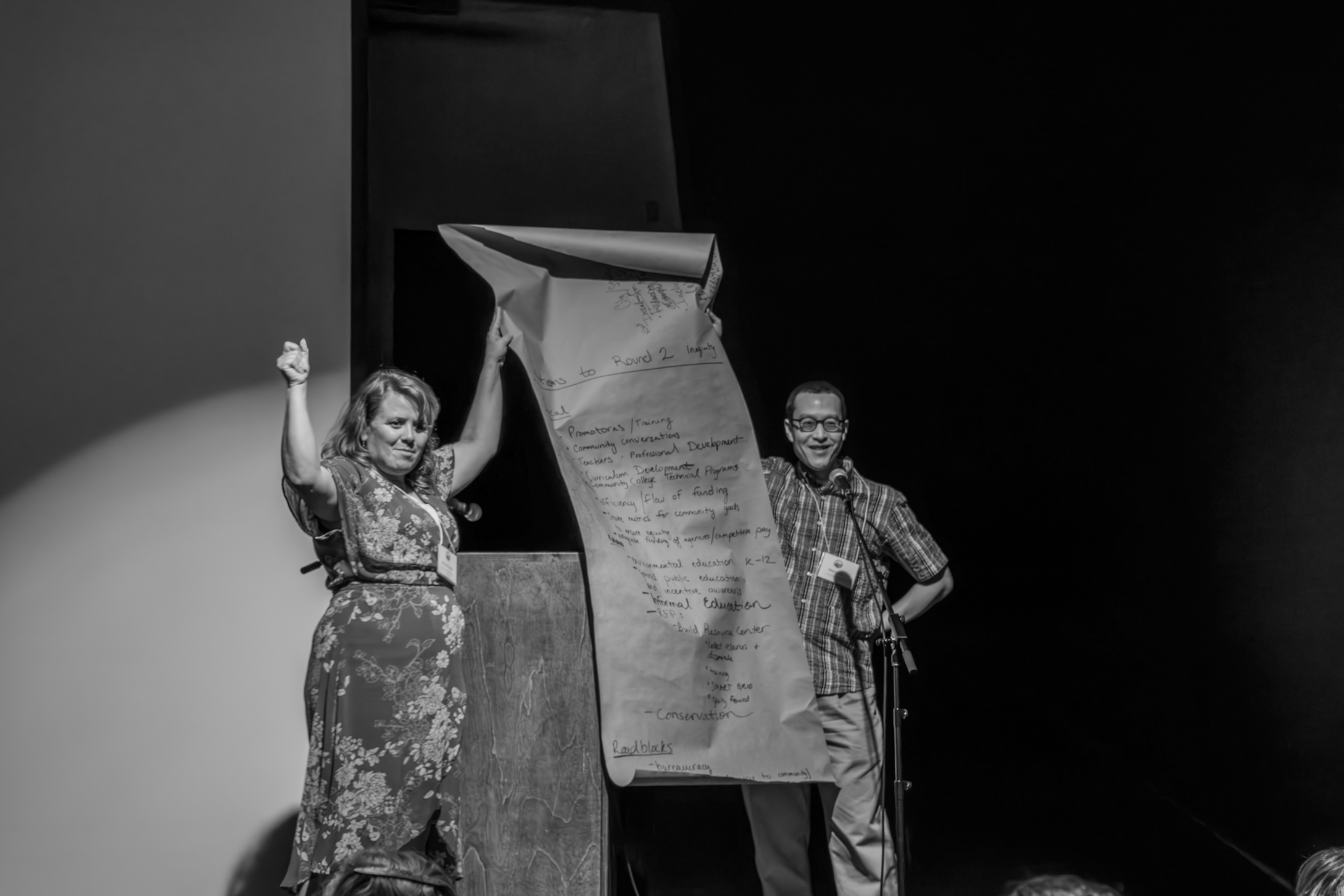 two people holding up a large paper on stage