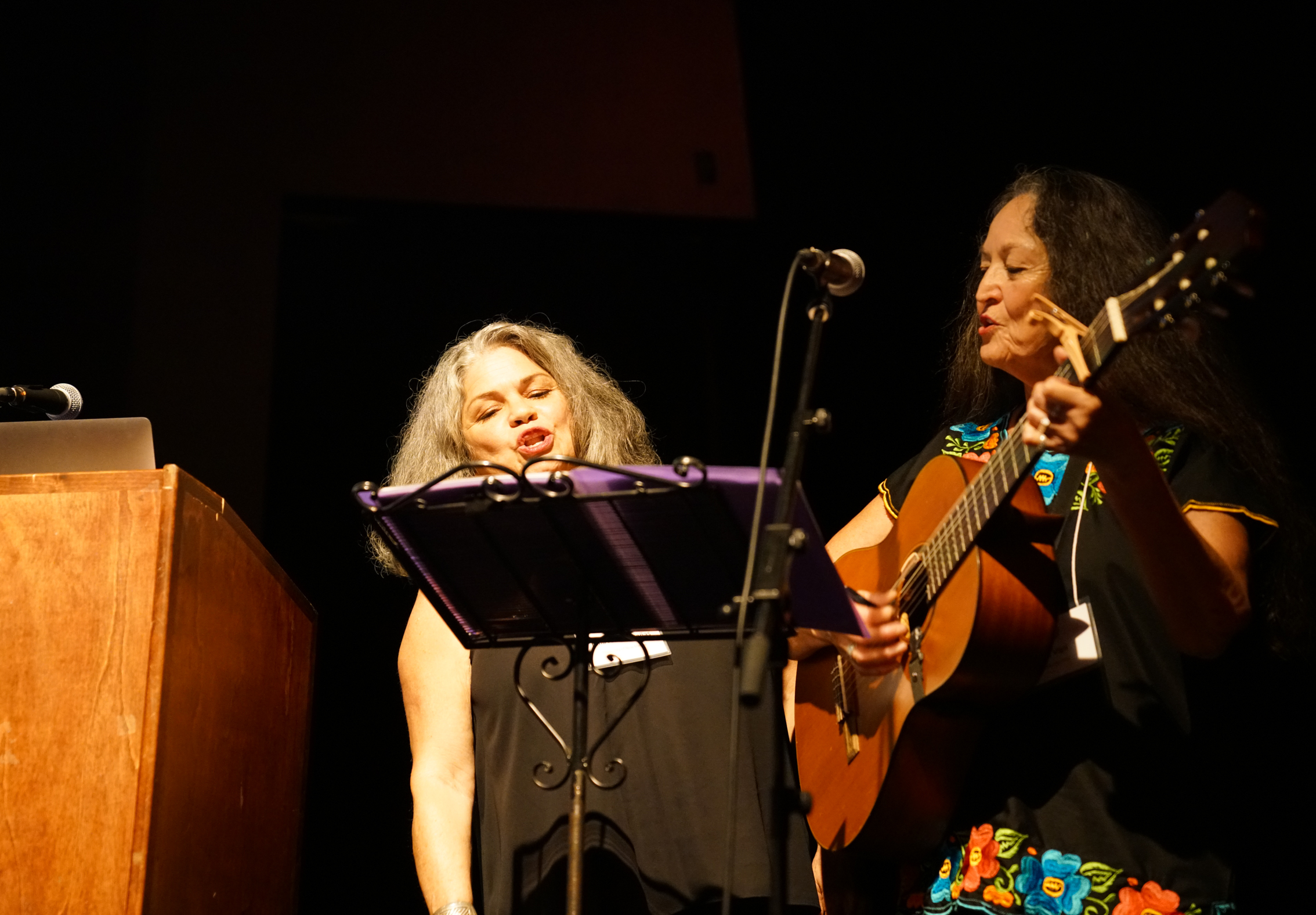 Two women standing at lectern playing guitar and singing